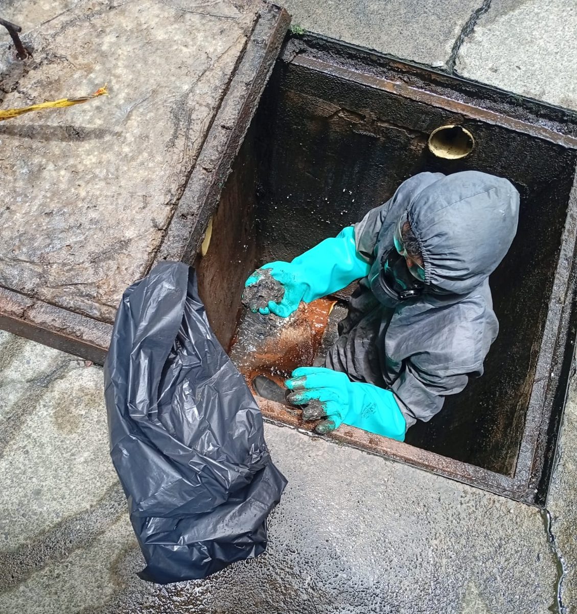 Operario con traje, guantes y máscara retirando lodos dentro de la caja