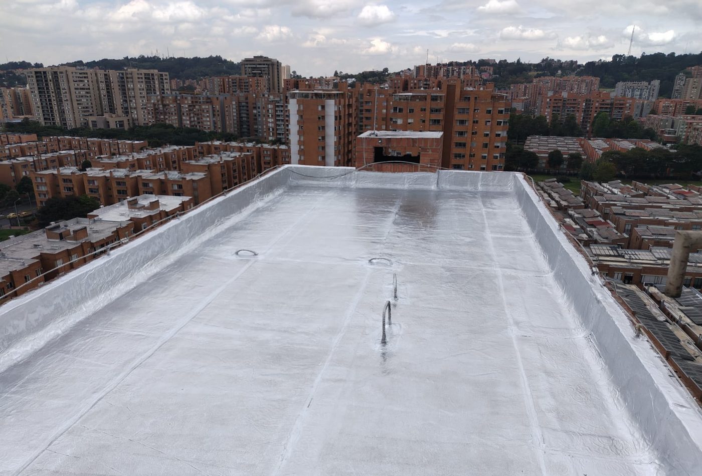 Cubierta plana impermeabilizada con acabado reflectivo, con edificios de Bogotá al fondo